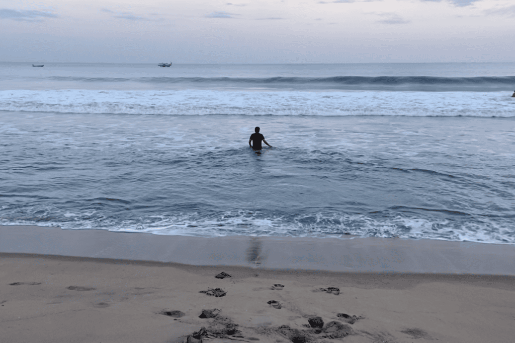 Pondicherry- beach Akash standing knee-deep in the ocean waters under a cloudy sky.