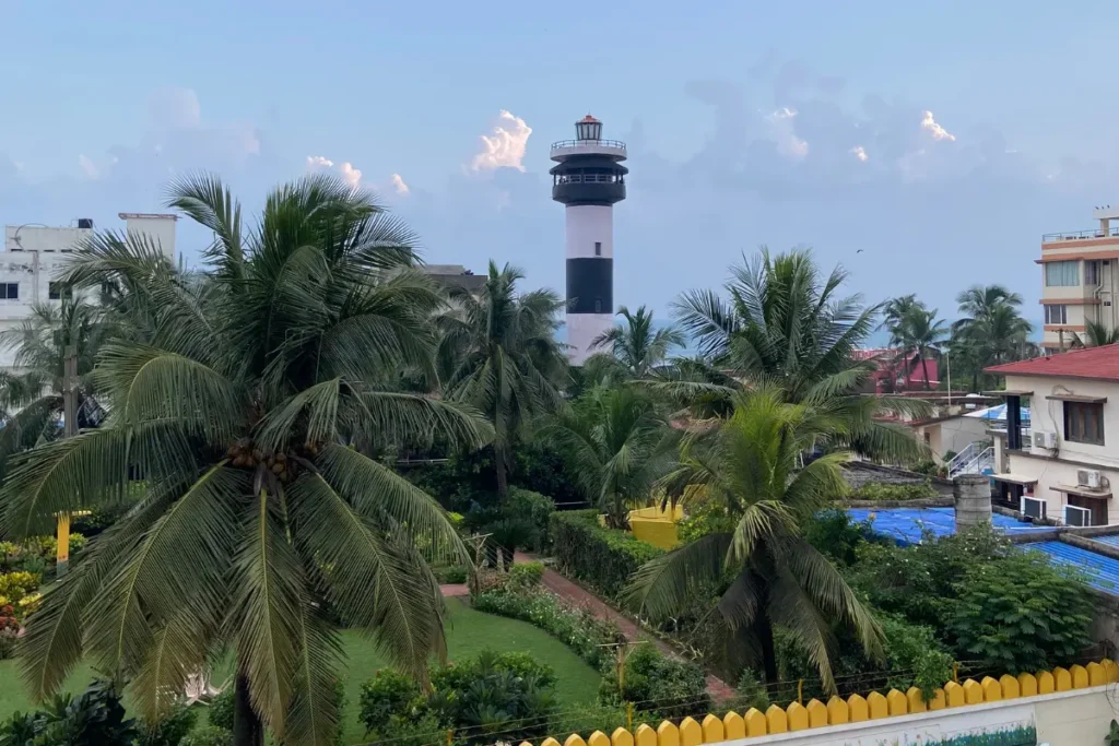 Puri- Light house A daytime shot looking out from a balcony at a black and white striped lighthouse rising above green palm trees.