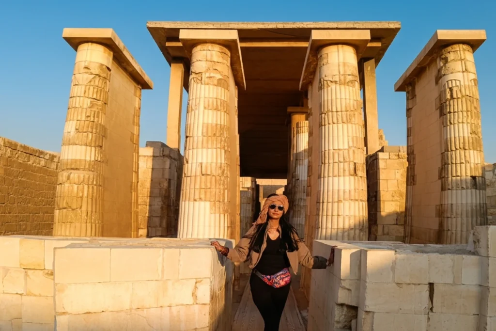 SAQQARA- 2 Sumana smiles while posing for a photo directly in front of the towering stone entrance pillars of the complex.