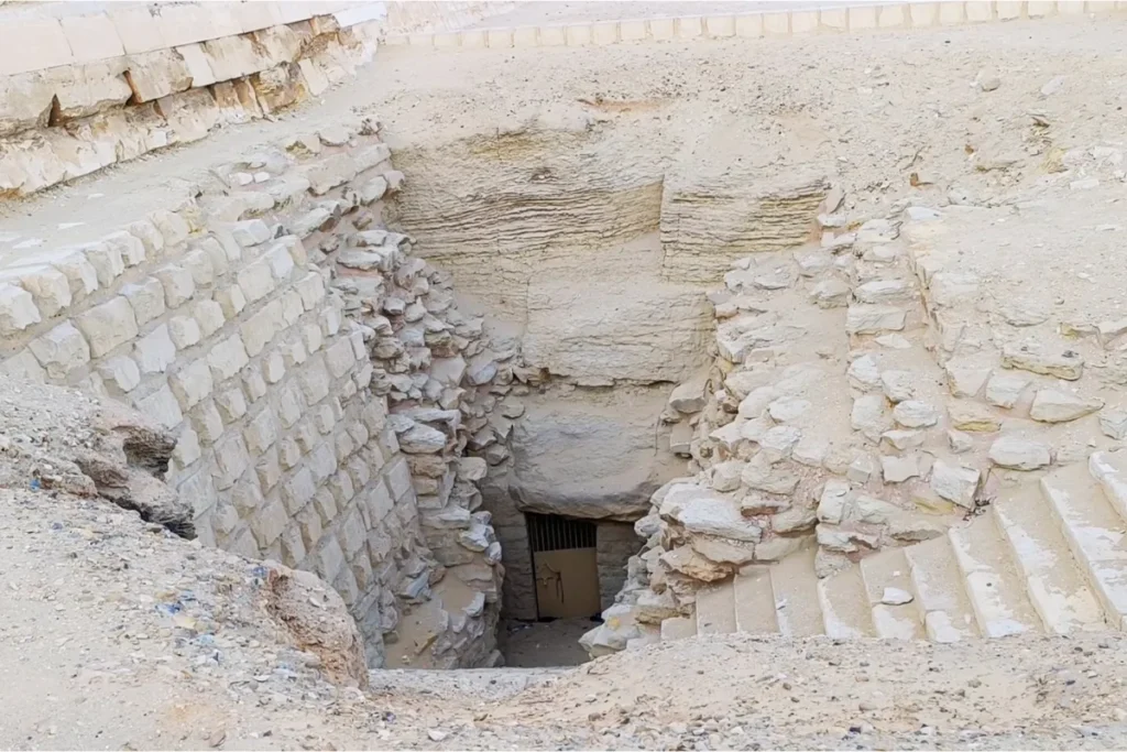 SAQQARA- 3 Looking down into a deep, rectangular stone pit or excavation site that leads to an subterranean entranceway.