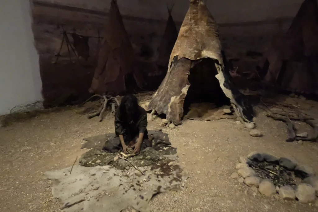 A museum diorama depicting early prehistoric human life inside a cave setting with figures and simple tools.