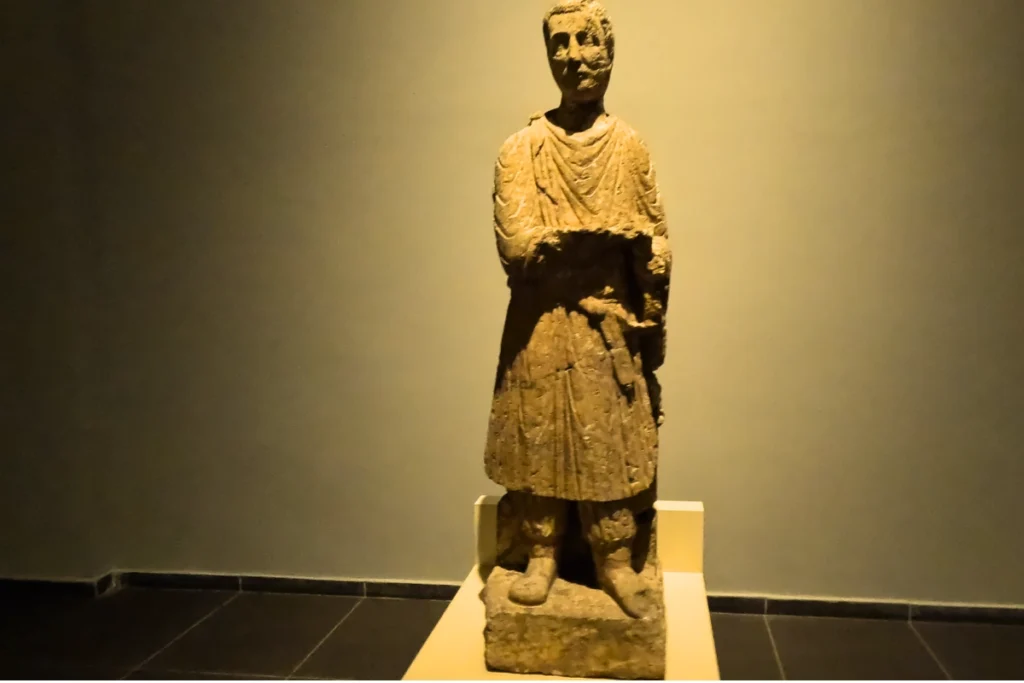 A classical carved stone statue of a Roman figure draped in robes standing on display.