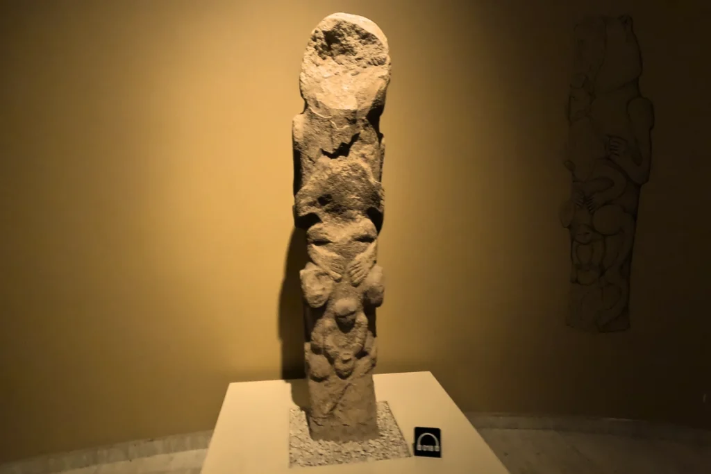 A detailed vertical view of an ancient carved stone totem pole depicting animal and human figures stacked together.