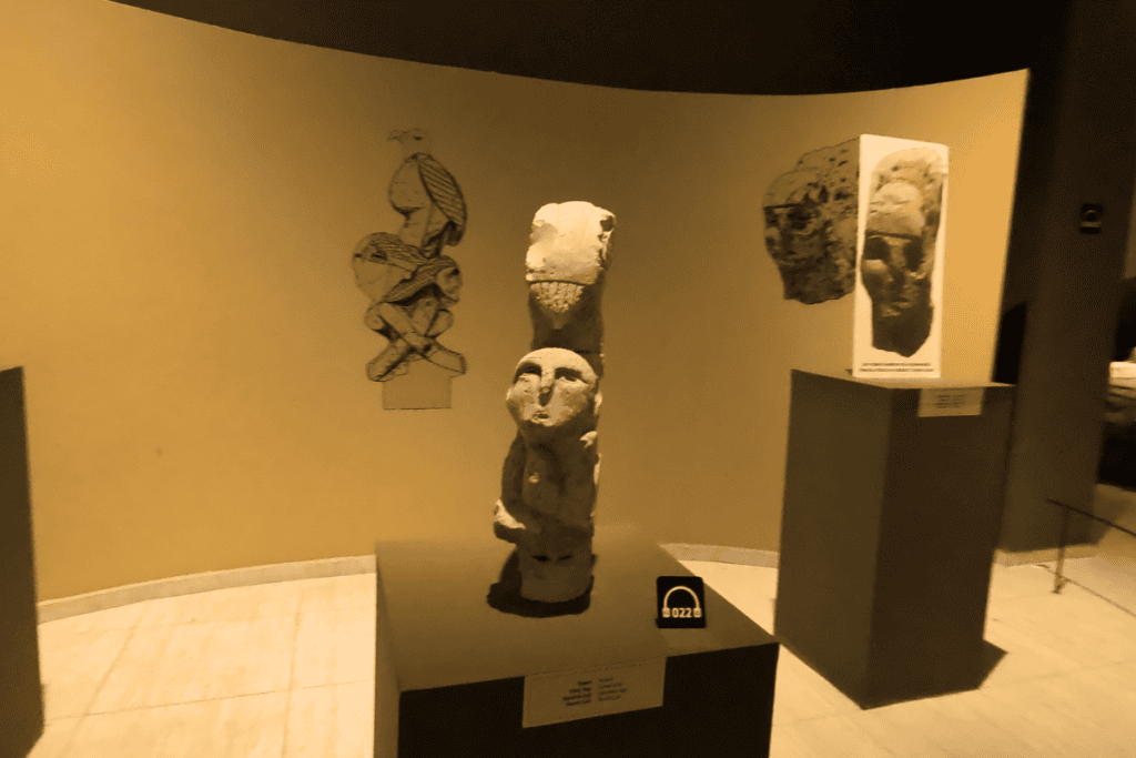 A carved stone totem pole featuring stacked figures including a predator animal at the top holding a human head.