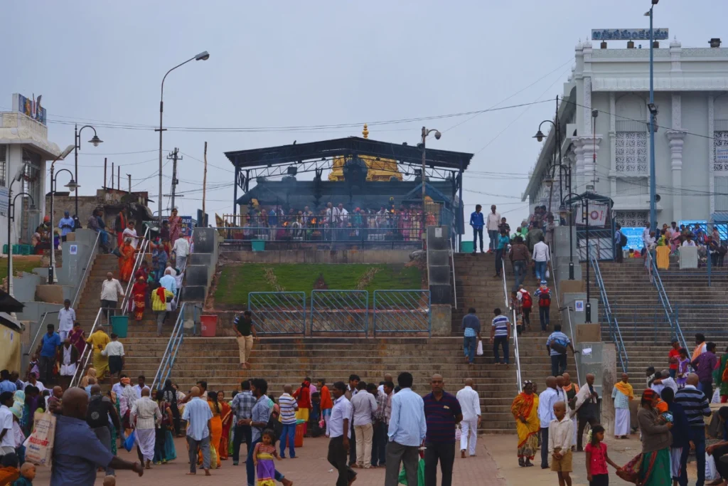 Tirupati- Coconut breaking point A busy stone staircase area filled with devotees, next to a dedicated stall or station labeled for offering coconuts.