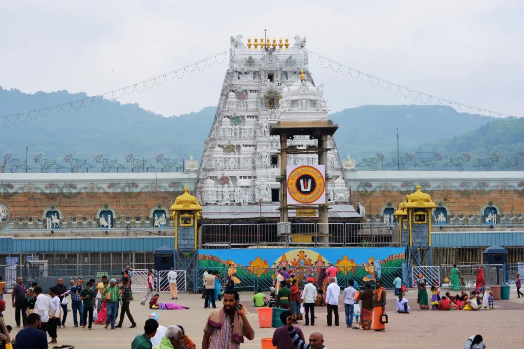 Tirupati- Temple A straight-on view of the massive white entrance tower of the temple complex, with people gathered on the plaza in front of it.