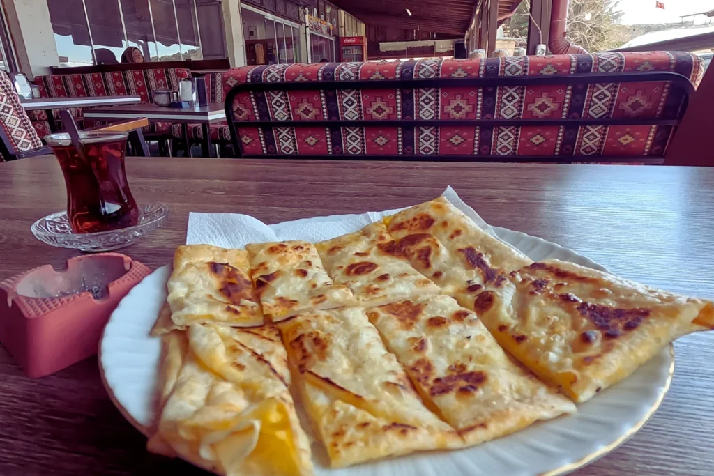Turkish Breakfast 4 A plate containing freshly made, sliced Gözleme flatbread served on a plate outdoors next to traditional cushions.