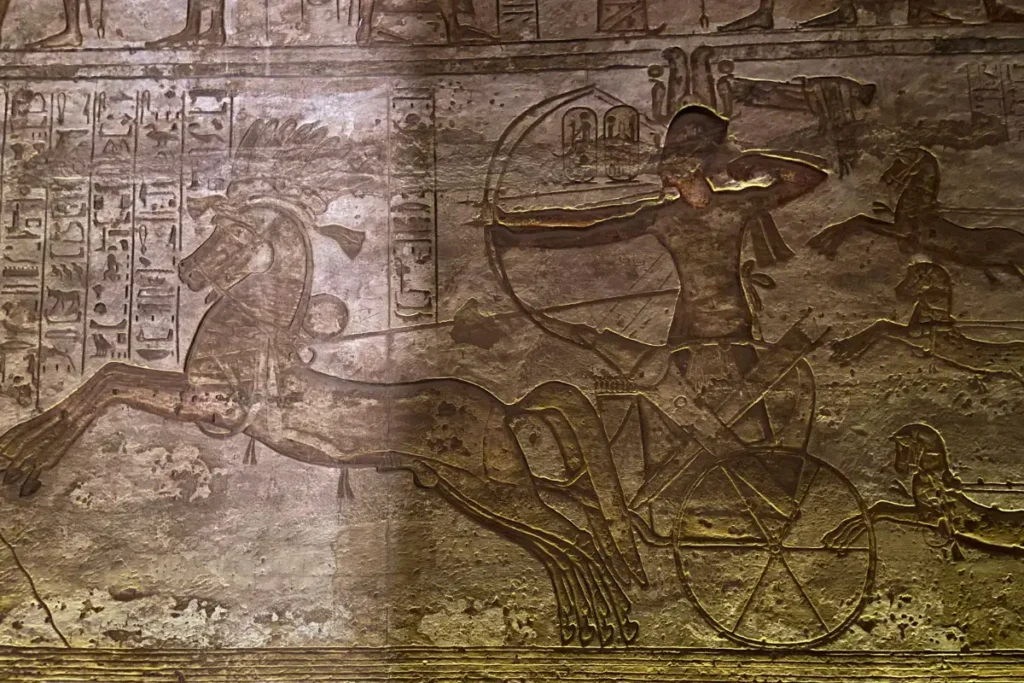 ABU SIMBEL Detailed ancient wall relief carving inside Abu Simbel depicting Pharaoh Ramesses II riding a horse-drawn chariot into battle.