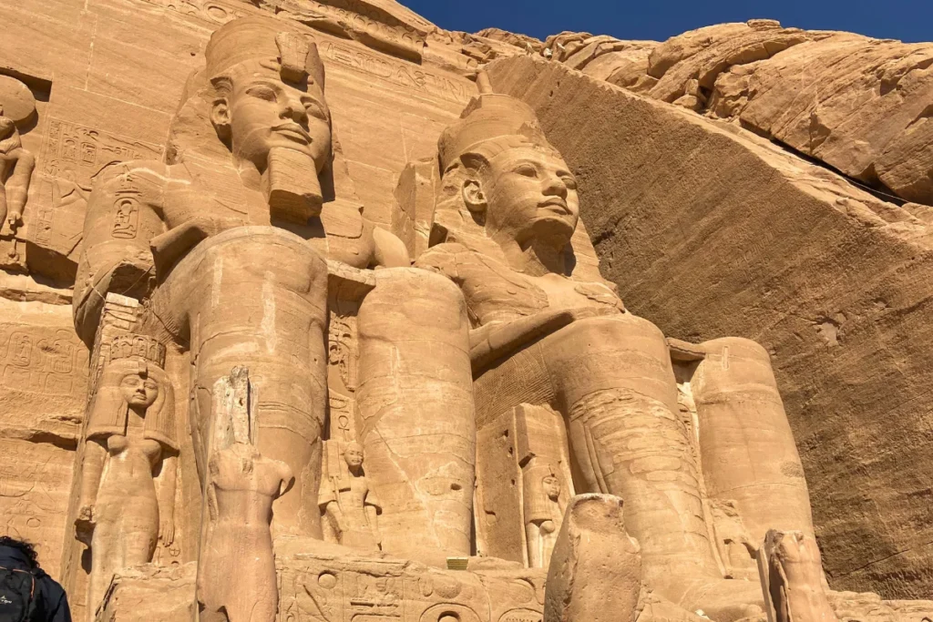 ABU SIMBEL 2 Close-up angled view of the towering seated statues of Ramesses II at the Great Temple of Abu Simbel under a clear blue sky.