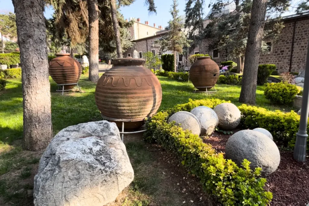 Anatolian Museum 1 Large ancient terracotta storage jars and spherical stone cannonballs resting on grassy ground in an outdoor garden courtyard.