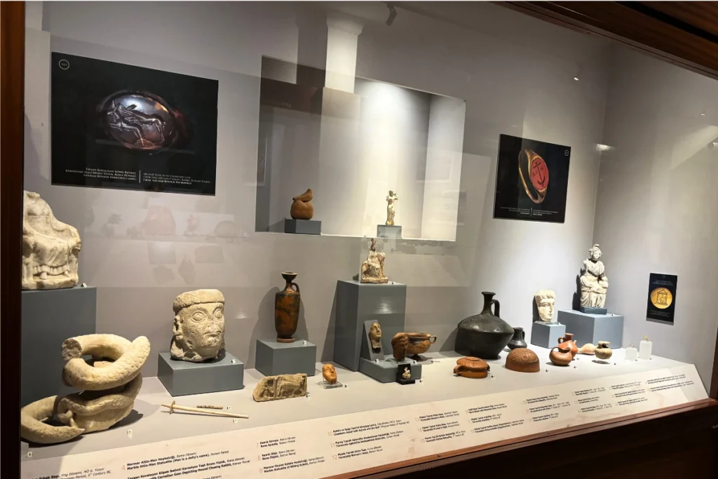 Anatolian Museum 14 A glass museum cabinet showcasing ancient terracotta vases, ceramic pottery, and small classical sculptures under display lights.