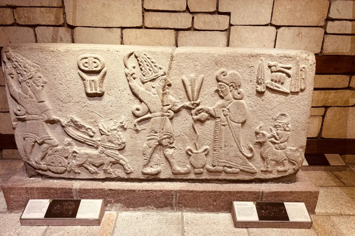 A close-up view of an ancient carved stone relief showing two Hittite figures standing face-to-face alongside chariot and animal carvings.