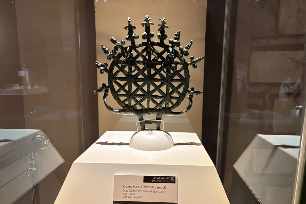 Anatolian Museum 8 An intricate, ancient bronze Hittite sun disk ceremonial standard mounted in a brightly lit glass exhibition case.
