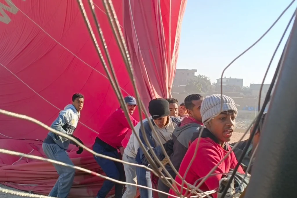 Egypt- Hot Air Balloon 10 Local ground crew members pulling ropes to secure a deflating red hot air balloon after landing.