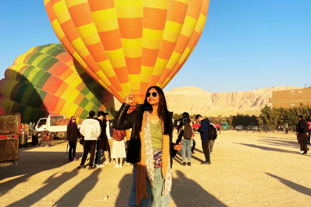 Egypt- Hot Air Balloon 5 Sumana posing outdoors with colorful inflated hot air balloons and other tourists in the background.
