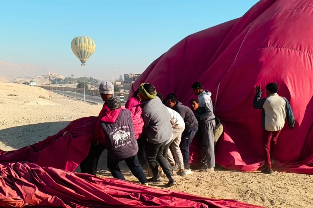 Egypt- Hot Air Balloon 8 Local ground crew members pulling ropes to secure a deflating red hot air balloon after landing.