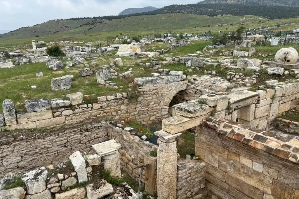 HIEROPOLIS - The Ploutonion 1 A wide elevated perspective of the excavated Ploutonion sanctuary complex and stone walls under bright sunlight.