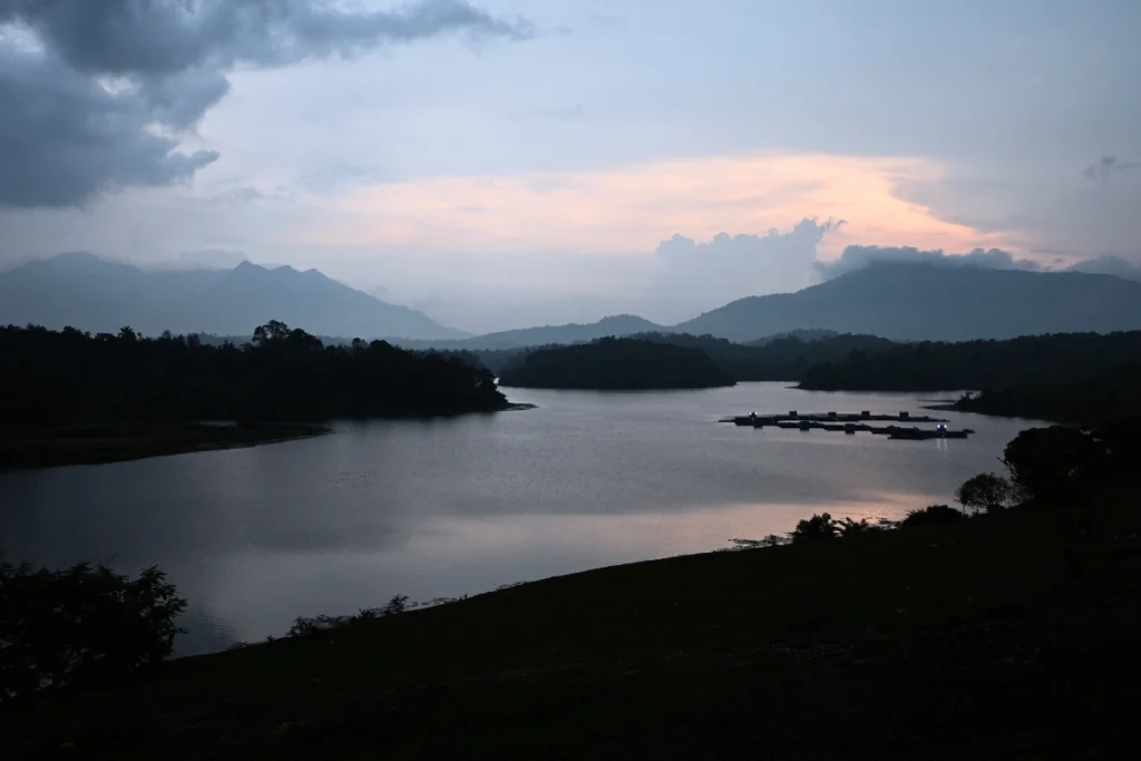 NELLARACHAL VIEW POINT Silhouette of mountains and trees against a dramatic sunset sky reflected on the calm surface of a reservoir lake.