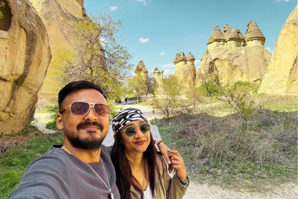 Pasabag Valley 2 Akash & Sumana taking a selfie outdoors in front of the iconic mushroom-shaped multi-capped fairy chimneys of Paşabağ Valley.