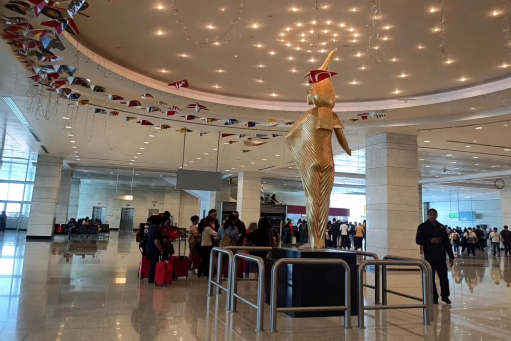 CAIRO Airport Wide shot of the spacious airport interior with traveler crowds, structural columns, and a central golden sculpture standing on a display platform.
