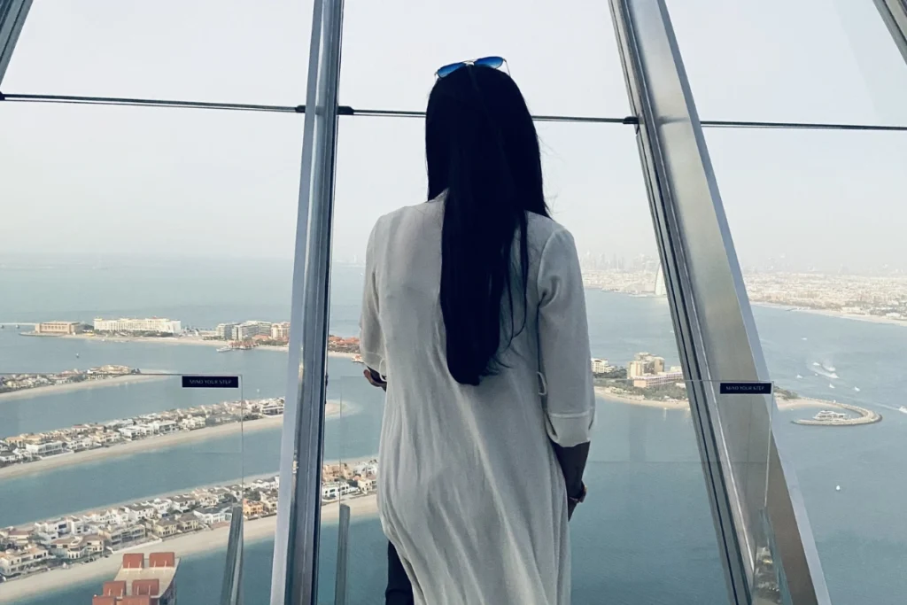 Dubai- Palm 2 Sumana looking through the glass of an observation deck toward Palm Jumeirah.