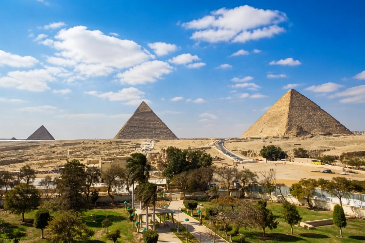 Panoramic view of the ancient Giza Pyramid complex with three large stone pyramids standing under a clear blue sky in Egypt.