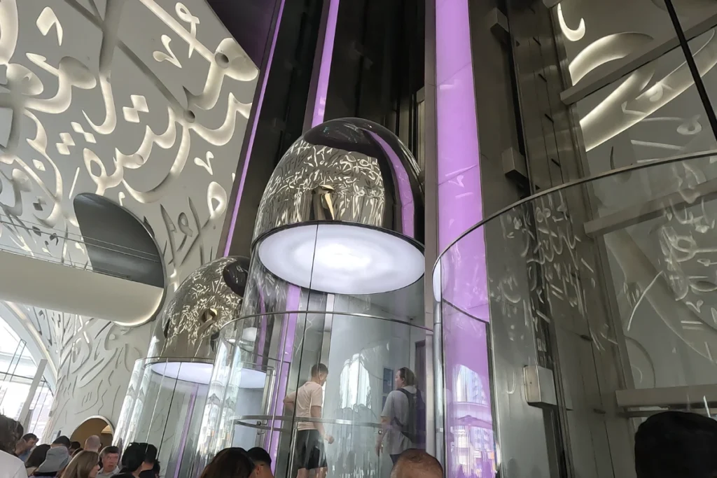 Museum of the future 8 Glass capsule elevator ascending through the central atrium surrounded by walls engraved with illuminated Arabic calligraphy.