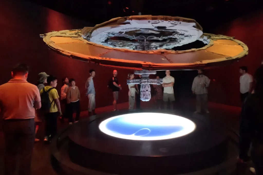 Museum of the future 9 Illuminated circular exhibit model depicting a futuristic orbital space station floating over Earth in a dark interactive room.
