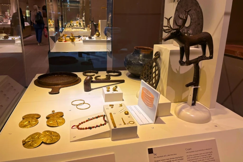 Alacahouk 7 Group of ancient bronze and gold artifacts, including sun discs and ornaments, displayed under museum lighting.