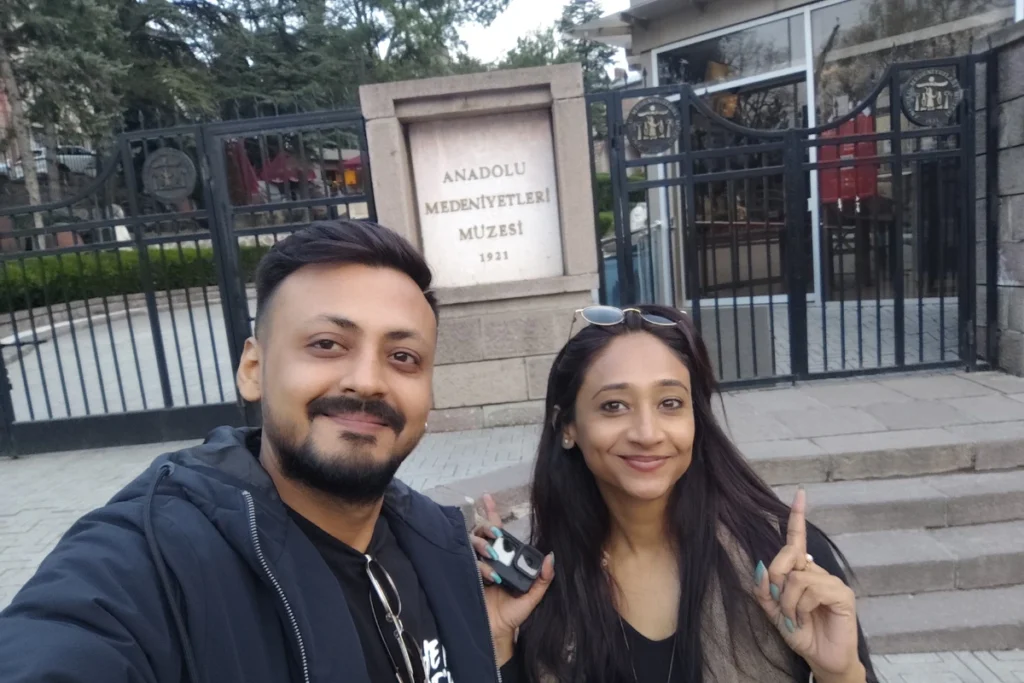 Ankara Museum Selfie of Akash & Sumana smiling outdoors in front of the stone entrance gates of the Museum of Anatolian Civilizations in Ankara.