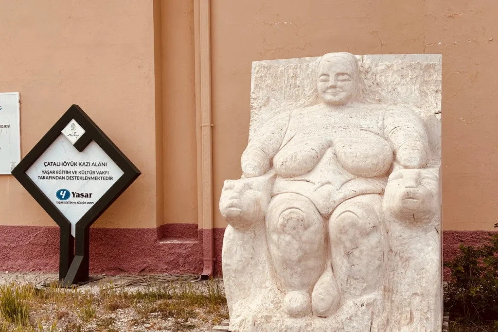 CatalHoyuk 8 A stone replica of the seated Mother Goddess sculpture positioned outdoors next to an information stand.