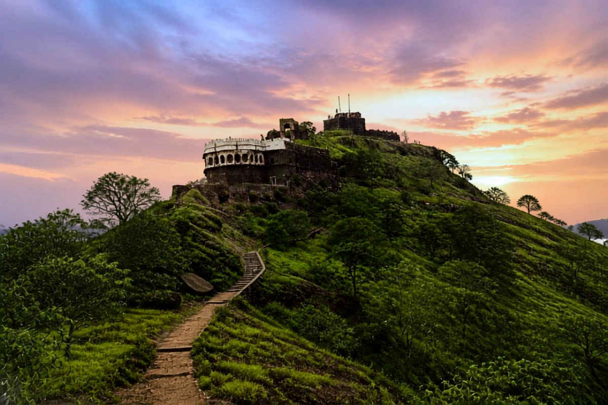 Panoramic view of Daulatabad Fort resting atop a green, conical hill under a cloudy sky.