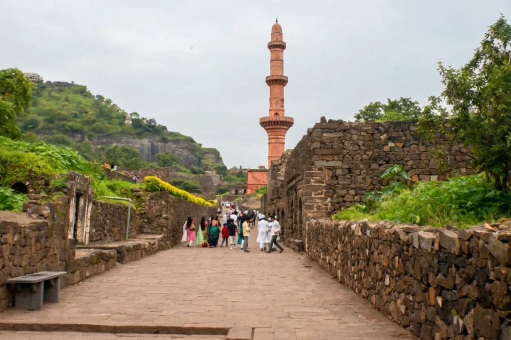 Daulatabad Fort 5 Tall, reddish-orange Chand Minar tower towering over stone walls and visitors walking along the paved fort path.