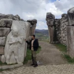 Panoramic view of the ancient stone gateway at Hattusa featuring the carved Hittite War God relief alongside Akash