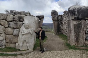 Panoramic view of the ancient stone gateway at Hattusa featuring the carved Hittite War God relief alongside Akash