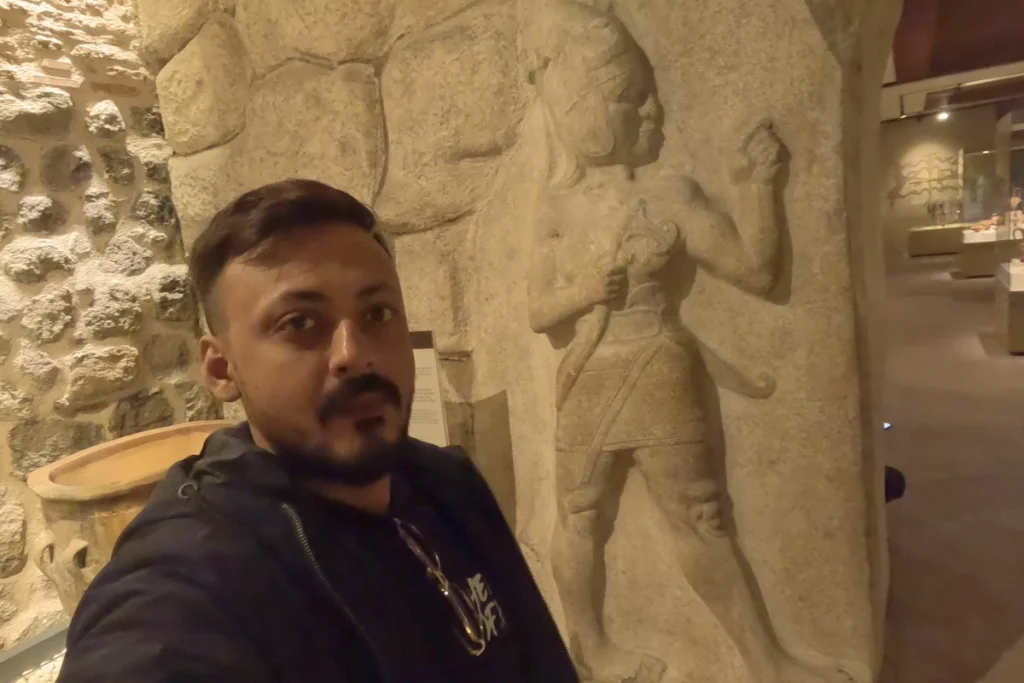 Akash standing next to the original limestone warrior relief displayed indoors at the museum.
