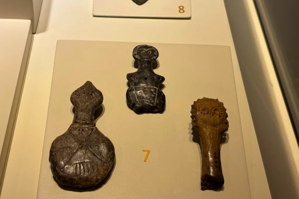Idol 4 Ancient carved stone idols in dark alabaster and marble displayed on a white shelf inside a glass showcase.