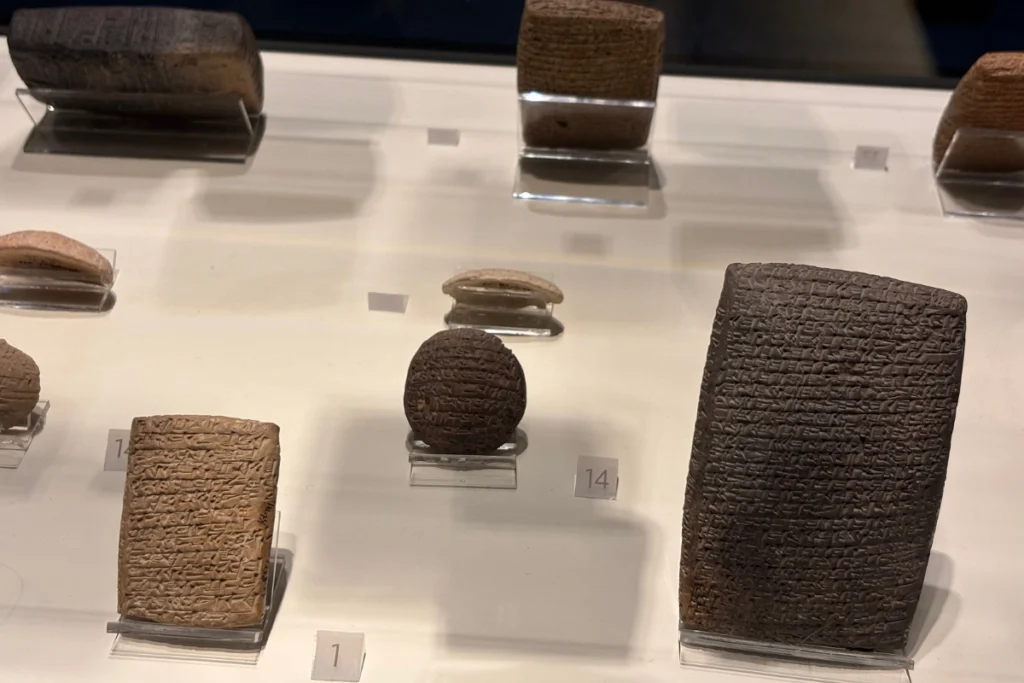 Kultepe Tablet 2 Collection of ancient cuneiform clay tablets and small terracotta artifacts displayed together on a museum shelf.