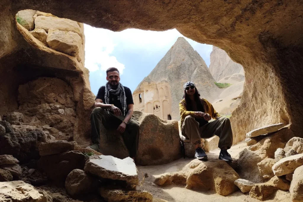 Selime Monastery 5 Akash & Sumana sitting in the shaded opening of a cave looking out through a natural rock archway at the surrounding landscape.